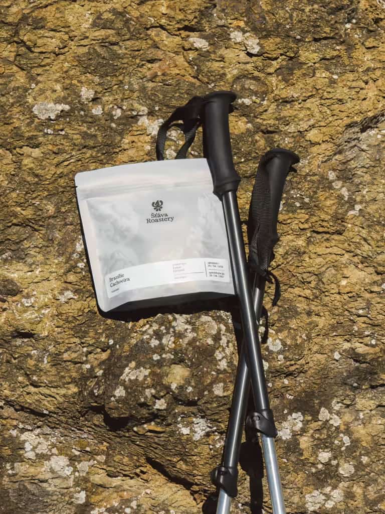 Sáček kávy Šťáva Roastery na skalách s turistickými holemi.